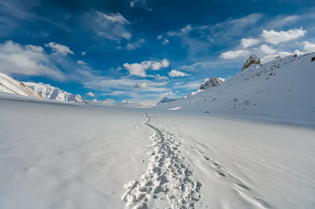 A line of footprints crossing a wide snowfield toward the mountains