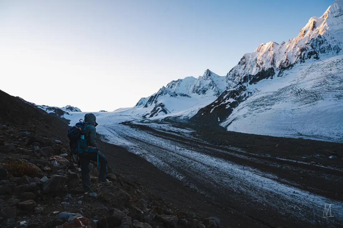 A trekker walking toward a glacier between snowy peaks
